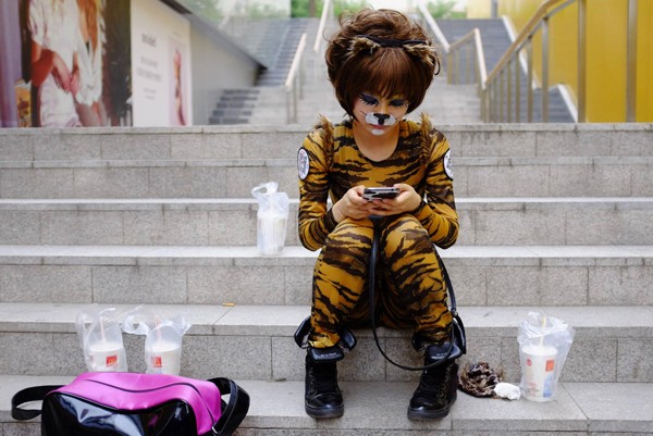 Une bénévole vêtu d'un costume de chien regarde son téléphone portable tandis qu'elle attend pour jouer dans un spectacle destiné à faire la promotion de l'amour des chiens, dans le quartier de Sanlitun à Beijing, le 20 juin 2013. [photo / agences]