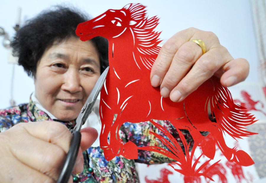 Cai Chun'e agée de 68 ans, une artiste dans l'art du papier découpé à Handan, la province de Hebei, montre son travail sur le thème du cheval, le 23 décembre 2013. Cai a récemment créé plus de 40 oeuvres dans différentes formes pour mettre en avant tout le charme de ce patrimoine culturel immatériel et souhaiter ses bons voeux pour l'Année du Cheval. [Photo : Hao Qunying/Asianewsphoto]